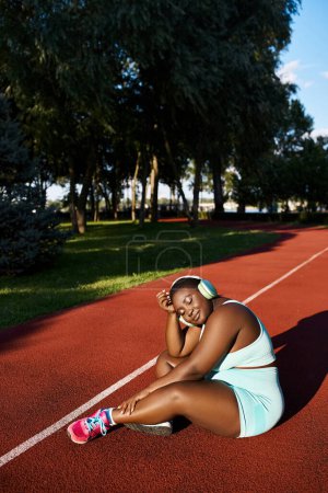 An African American woman in sportswear is sitting on a tennis court in headphones