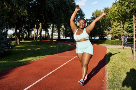 Une femme afro-américaine en tenue de sport court sur une piste avec des arbres en arrière-plan, mettant en valeur sa forme corporelle positive et incurvée.