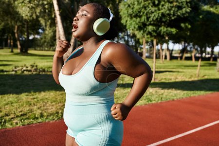 A body-positive African American woman in sportswear stands on a tennis court wearing headphones while enjoying music.