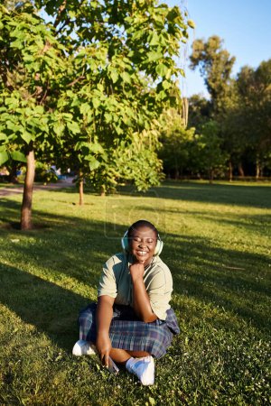 A plus size African American woman in casual clothing sitting peacefully on the grass outdoors on a sunny summer day.