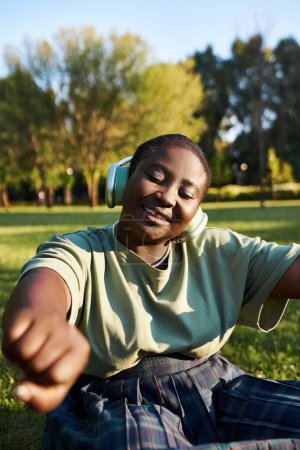 woman relaxes in the grass, immersed in music playing through headphones on a sunny day.