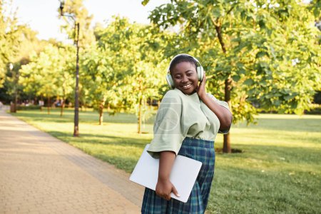 Photo for A plus-size African American woman in casual attire, wearing a green shirt and plaid skirt, outdoors in the summer. - Royalty Free Image
