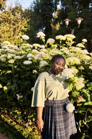 Plus-Size-Afroamerikanerin steht im Sommer selbstbewusst vor einem bunten Blumenstrauch.