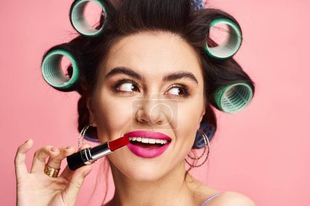 Woman with curlers in hair holds lipstick in front of face.