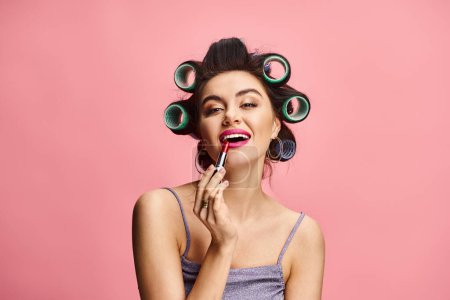 Photo for A woman with curlers on her head applying lipstick. - Royalty Free Image