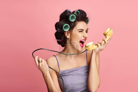 Stylish woman in curlers posing with retro phone.