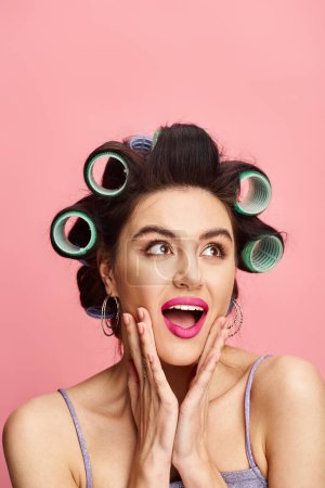 A woman with curlers in her hair poses against a vibrant backdrop.