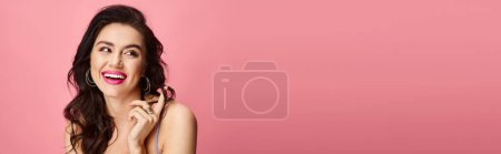Natürliche Schönheit mit langen dunklen Haaren posiert vor einem leuchtend rosa Hintergrund.