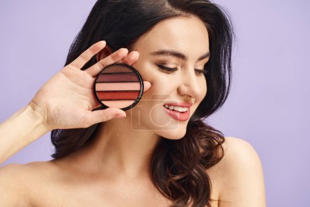 Mujer atractiva con belleza natural sostiene una paleta y se aplica maquillaje.