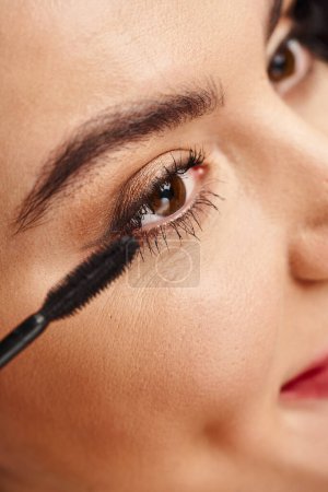 Retrato de cerca de una mujer atractiva que se maquilla con un rímel cerca del ojo.
