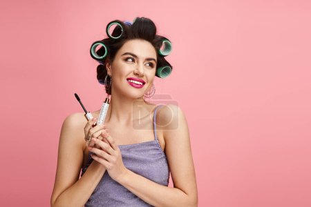 Stylish woman with curlers in hair holds mascara, applying makeup with precision.