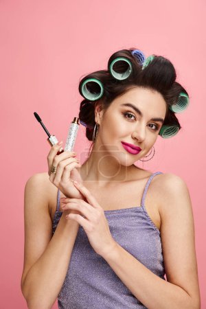Photo for A woman with curlers in her hair applies mascara. - Royalty Free Image