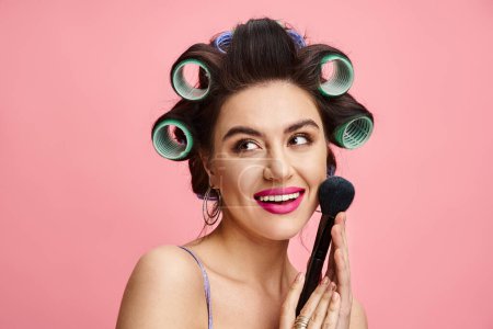 A woman with curlers in her hair holds a brush, showcasing her beauty routine.