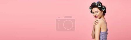 Téléchargez les photos : Femme avec des bigoudis dans les cheveux, debout élégamment sur fond rose. - en image libre de droit