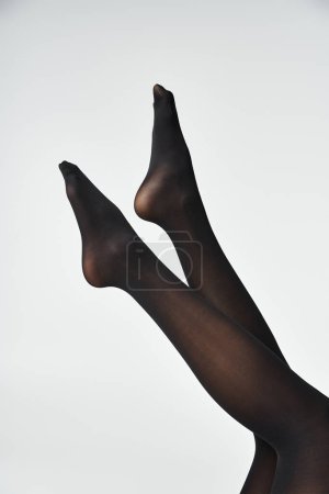 Foto de Una joven mostrando sus piernas en medias negras sobre un fondo gris de estudio. - Imagen libre de derechos