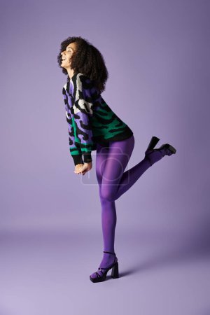 Photo for A young woman poses in tights and a green and black jacket against a purple background in a studio setting. - Royalty Free Image