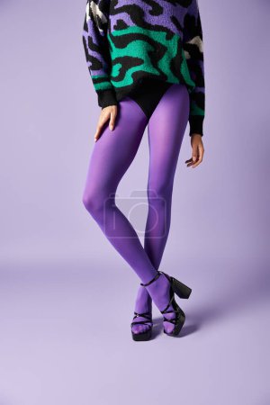 Foto de Mujer joven vestida con medias púrpura vibrante y un suéter que golpea una pose en un estudio sobre un telón de fondo púrpura. - Imagen libre de derechos