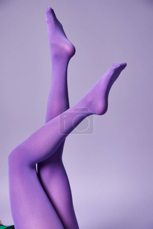 Foto de Una joven muestra sus piernas en medias vibrantes sobre un fondo púrpura en un estudio. - Imagen libre de derechos