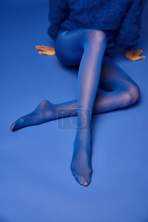 Téléchargez les photos : Une jeune femme élégamment posée en collants et pull bleu vif sur un fond frappant. - en image libre de droit