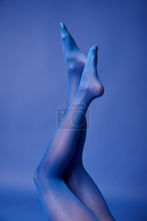 Die Beine einer jungen Frau werden elegant durch blaues Licht hervorgehoben, sie trägt eine lebhafte Strumpfhose und einen Pullover und posiert in einem Studio.