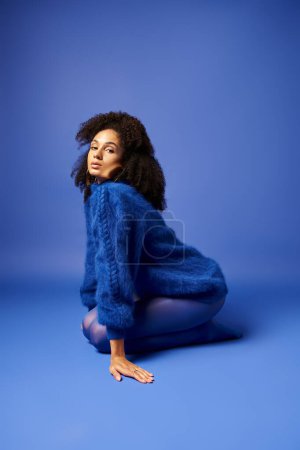 Eine junge Frau in leuchtenden Strumpfhosen und Pullover sitzt auf dem Boden vor auffallend blauem Hintergrund.