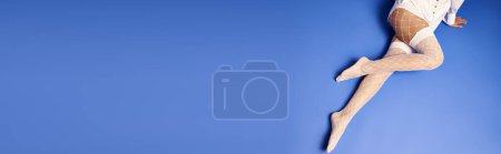 Téléchargez les photos : Une jeune femme en chemise blanche et collants s'envole gracieusement dans les airs sur un fond bleu dans un décor studio. - en image libre de droit