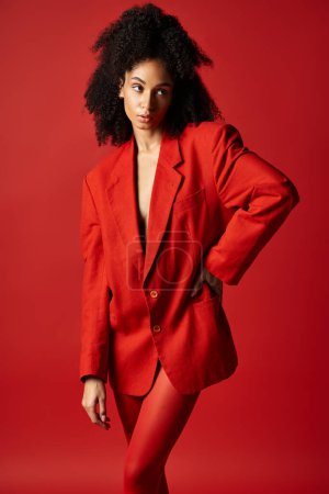 Photo for A young woman in a vibrant red suit strikes a confident pose for a photograph in a studio setting. - Royalty Free Image