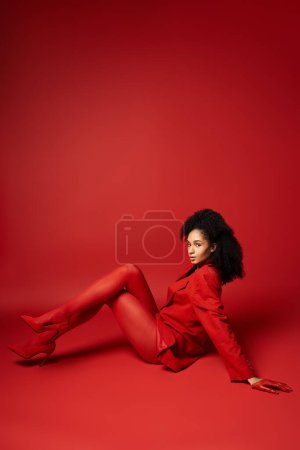 A young woman in a striking red outfit is gracefully laying on the floor against a vibrant background in a studio setting.