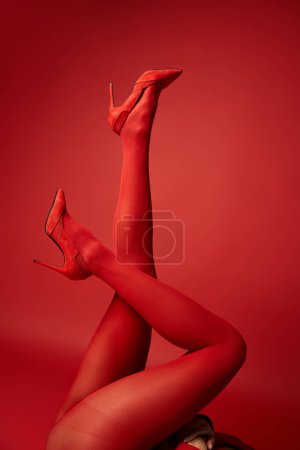 A young woman confidently struts in red stockings and high heels against a vibrant studio backdrop.
