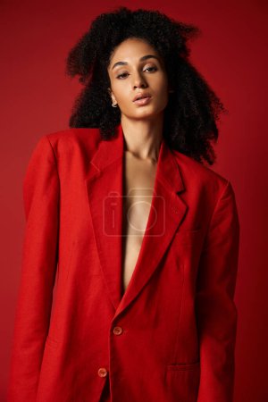 Foto de Una joven mujer emana confianza y aplomo mientras posa en un elegante traje rojo sobre un vibrante fondo de estudio. - Imagen libre de derechos