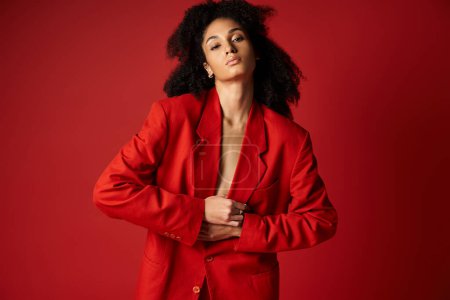 Téléchargez les photos : Une jeune femme en costume rouge saisissant pose pour une photo sur un fond de studio dynamique. - en image libre de droit