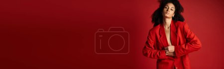 Téléchargez les photos : Une jeune femme en costume rouge vibrant se tient en confiance devant un mur assorti. - en image libre de droit