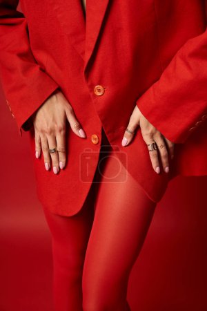Photo for A stylish young woman stands confidently in a red suit and matching stockings against a vibrant studio background. - Royalty Free Image