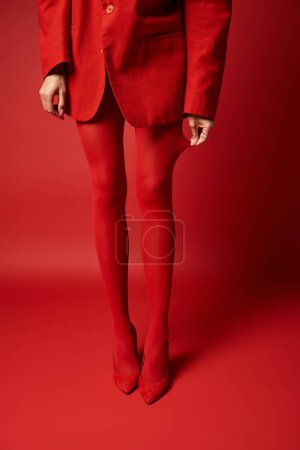 Foto de Una mujer joven y elegante está vestida con un llamativo traje rojo y medias a juego contra un vibrante telón de fondo de estudio. - Imagen libre de derechos