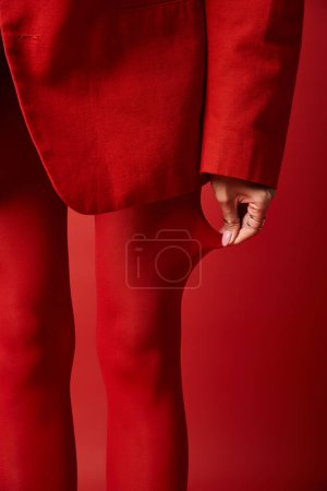 A young woman in a red suit and red tights strides confidently against a vibrant background in a studio.