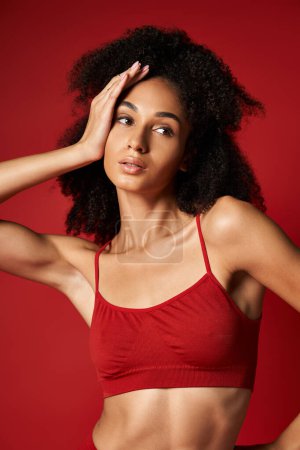 Mujer joven vibrante posa con confianza en un llamativo sujetador deportivo rojo para una sesión de fotos con estilo. Configuración del estudio.