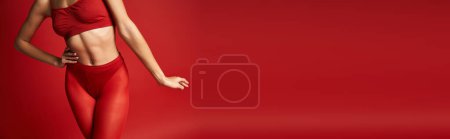 Eine junge Frau strahlt in einem leuchtend roten Bikini-Top und passenden Leggings im Studio Zuversicht aus.