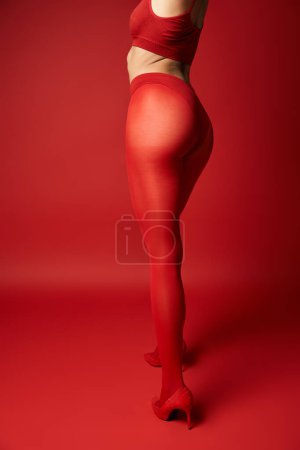 Téléchargez les photos : A young woman stands confidently in a red top and tights against a vibrant background in a studio setting. - en image libre de droit