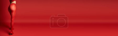 Téléchargez les photos : A young woman in a striking red dress stands confidently on a vibrant red surface. - en image libre de droit