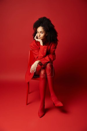 Téléchargez les photos : Une jeune femme élégante dans une robe rouge vibrante s'assoit gracieusement sur une chaise assortie. - en image libre de droit