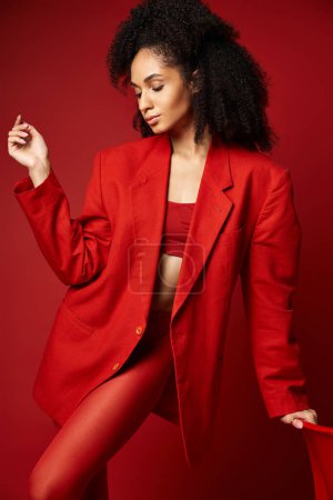 A young woman confidently strikes a pose in a vibrant studio setting, dressed in a striking red suit.
