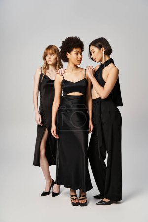 A diverse group of elegant women of Caucasian, Asian, and African American descent standing next to each other on a grey studio background.