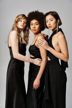Foto de Tres hermosas mujeres multiculturales se paran elegantemente juntas en un estudio sobre un fondo gris. - Imagen libre de derechos