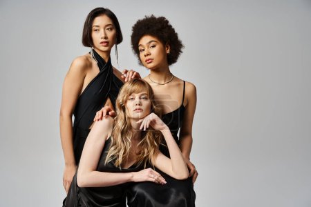 Photo for Three diverse women wearing black dresses strike a pose against a grey background in a studio setting. - Royalty Free Image