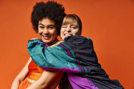 Zwei Frauen verschiedener Rassen stehen vor orangefarbenem Hintergrund zusammen und umarmen die Schönheit des Frühlings.