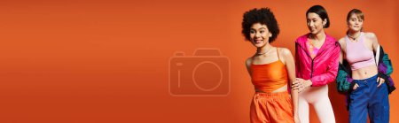 Téléchargez les photos : Groupe de femmes diverses, y compris caucasiennes, asiatiques et afro-américaines, se tiennent unis dans un contexte de studio orange. - en image libre de droit