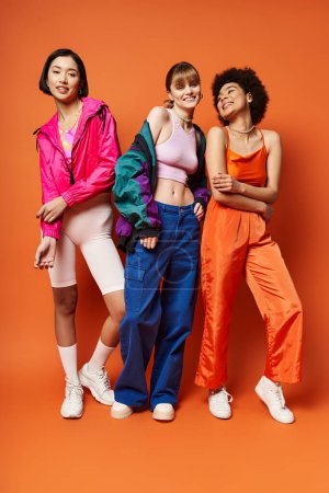 Foto de Un grupo multicultural de hermosas mujeres jóvenes de pie juntas sobre un fondo naranja. - Imagen libre de derechos