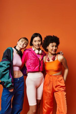 Un groupe diversifié de femmes, y compris caucasiennes, asiatiques et afro-américaines, se tiennent gracieusement ensemble dans un contexte de studio orange.