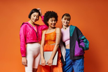 Tres mujeres diversas - caucásicas, asiáticas, afroamericanas - se unen contra un fondo de estudio naranja, irradiando belleza y unidad.
