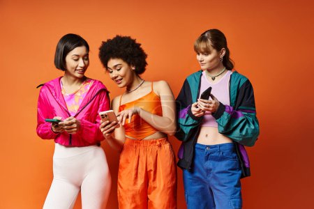 Tres mujeres multiculturales de pie juntas, absortas en sus teléfonos.